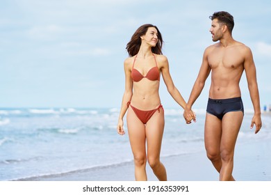 Junge Paar schöne Sportler gehen Hand für Hand am Strand spazieren und genießen ihren Urlaub auf See