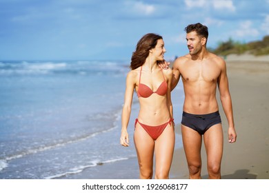 Junge Paar wunderschöne Sportler, die zusammen am Strand spazieren und ihren Urlaub auf See genießen