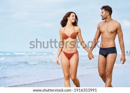 Young couple of beautiful athletic bodies walking together hand by hand on the beach enjoying their holiday at sea