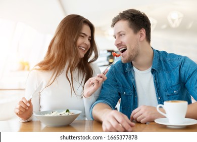 young couple beautiful woman feeds her smioling handsome man with salad drinking coffee in cafe looking happy, relationship concept