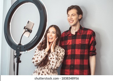 Young Couple Of Beauty Bloggers, Hair Stylist, Hairdresser And Model With Hair Style Shoot On Mobile Phone With Ring Lamp On Grey Wall Background