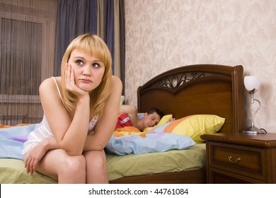 Young Couple In A Bed Bored Woman. Woman And Man Having A Disagreement. Male Is Sleeping And Female With Sad Expressions.