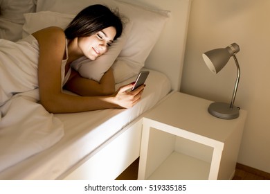 Young Couple In Bed. Man Sleeps While A Young Woman Looking Phone At Night