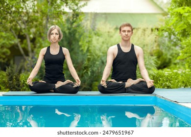 Young couple in black attire meditating in lotus position on poolside. Perfect for wellness, fitness, and lifestyle themes. Ideal for promoting yoga retreats, mindfulness apps, or health magazines. - Powered by Shutterstock