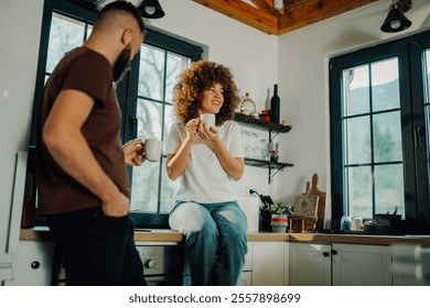 Young couple bonds over coffee in their cozy kitchen, chatting and enjoying a warm beverage as sunlight fills the room, capturing a simple moment of togetherness in their loving relationship - Powered by Shutterstock