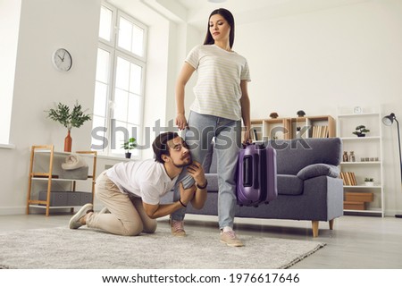 Young couple breaking up. Woman with packed bag leaving home. Funny clingy traitor husband on floor holding wife's leg imploring her to give second chance. Relationship breakup and divorce concept Foto stock © 