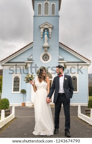 young couple bride groom getting married wedding posed photos at blue christian church hairpiece flowers bouquet 