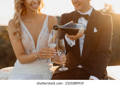 young couple, bride and groom, spend romantic evening after wedding day on rooftop against backdrop of city, man carefully pours champagne or wine into glasses. Happy wedding day together for two. - Powered by Shutterstock