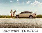 The young couple broke down the car while traveling on the way to rest. They are trying to fix the broken by their own or should hitchhike, getting nervous. Relationship, troubles on the road