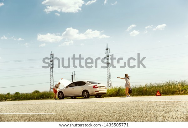 The young couple broke down the car while\
traveling on the way to rest. They are trying to stop other drivers\
and ask for help or hitchhike. Relationship, troubles on the road,\
vacation.
