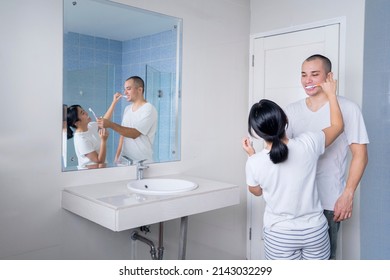 Young Couple Brushing Teeth Each Other While Standing Together In Front Of A Mirror In Bathroom. Shot At Home