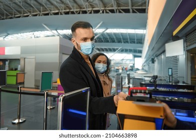 Young Couple Of Business Partners In Protective Medical Masks, Traveling During Pandemic, Standing At The Check-in Counter, Passing Customs And Passport Control At The Airport Terminal. Copy Ad Space