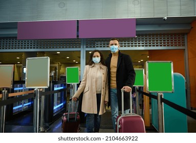 Young Couple Of Business Partners In Protective Medical Masks, Standing With Suitcases At Check-in Counter, Waiting For Check-in, Passing Customs And Passport Control In Airport Terminal. Copy Space