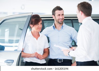 Young couple buying automobile from salesman in a car salon