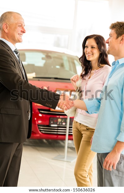 Young\
couple buying car from salesman shaking\
hands
