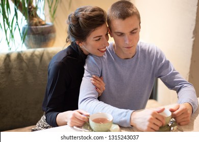 young couple in a cafe drinking coffee and hugging, young woman laughs