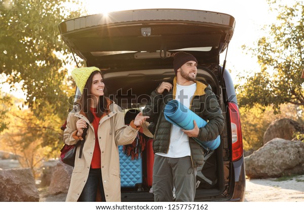 Young couple with camping equipment near car
trunk outdoors