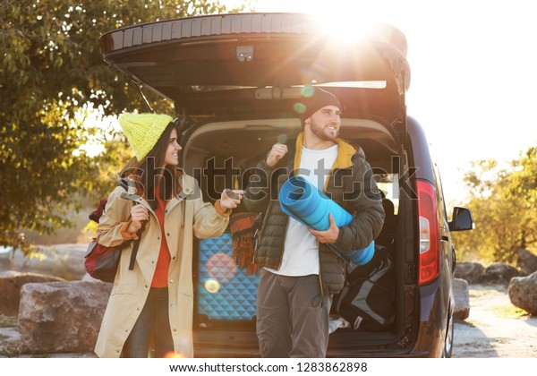 Young couple with camping equipment near car\
trunk outdoors