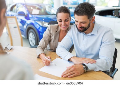 Young couple with car dealer in auto salon