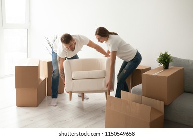 Young couple carry chair to new living room after moving in to shared apartment, husband and wife furnishing their first home, settling furniture, helping each other in renovation or interior design