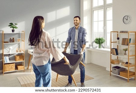 Young couple carrying armchair into their living room. Smiling man and woman moving into new apartment, furnishing and remodeling room. House improvement, remodeling concept