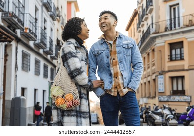 Young couple carrying a bag of groceries together on a lively urban street. - Powered by Shutterstock