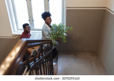 Young Couple Carrying Big Cardboard Box Into New Home. Moving House. Couple Carrying Boxes Up The Staircase While Moving Into A New Building. Young Happy Black Couple Relocating Into New Home.