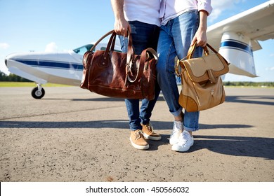 Junge Paare, die braune Ledertaschen im Flugzeug auf der Landebahn tragen. Mann und Frau, die auf einem Urlaubsflug sind, weißes Flugzeug auf dem Hintergrund. Sonniger Sommertag