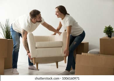 Young couple carrying chair together, house improvement, modern furniture in new home concept, man and woman moving into own flat after relocation furnishing living room, remodeling and renovation