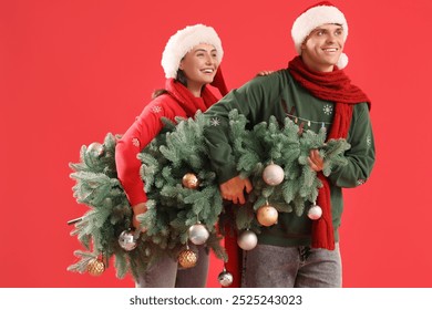 Young couple carrying Christmas tree on red background - Powered by Shutterstock