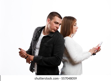 Young couple in casual wear standing back to back and using phone. Angry guy is jealous of his girlfriend to her life in social networks, white isolated background, copy space