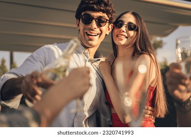 Young Couple Celebrating at Outdoor Party - A Caucasian couple, dressed in casual-elegant attire, embracing and smiling while the man pours champagne. - Powered by Shutterstock