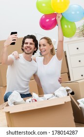Young couple celebrating their new home laughing and holding up a bunch of colorful party balloons as they take a self portrait on their smartphone for family and friends