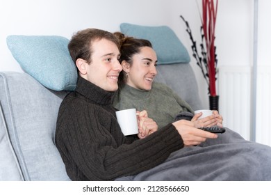 Young Couple Channel Surfing On Television While Taking A Warm Cup Of Coffee