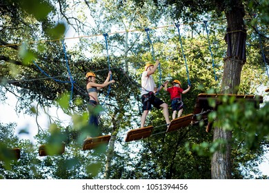 A Young Couple With A Child Walking On A Rope Bridge With Insurance. The Concept Of Active Family Rest, Spot