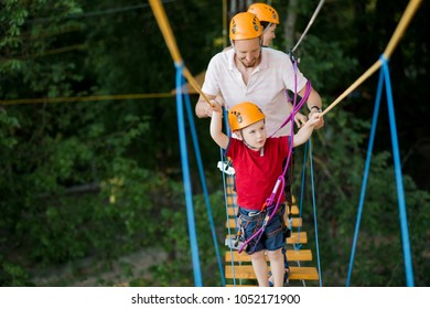 A Young Couple With A Child Walking On A Rope Bridge With Insurance. The Concept Of Active Family Rest, Spot