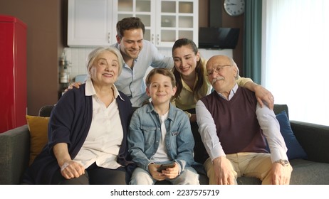 Young couple with children, their son and elderly parents sitting on sofa in living room, taking self portraits together. Portrait of happy cheerful big family smiling at camera in cozy living room. - Shutterstock ID 2237575719