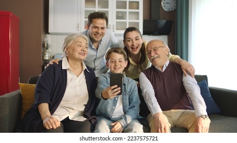 Young couple with children, their son and elderly parents sitting on sofa in living room, taking self portraits together. Portrait of happy cheerful big family smiling at camera in cozy living room. - Shutterstock ID 2237575721