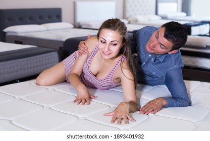 Young Couple Choosing And Lying At Matress In Furniture Store