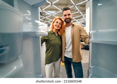 Young Couple Choosing A Refrigerator In A Home Appliances And Electronics Store. Inside View. Buying A New Refrigerator.