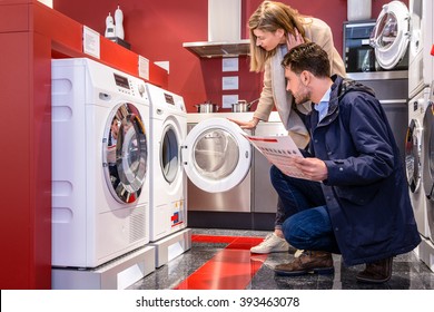 Young couple choosing washing machine in household appliance section at hypermarket