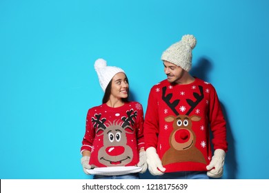 Young couple in Christmas sweaters and knitted hats on color background
