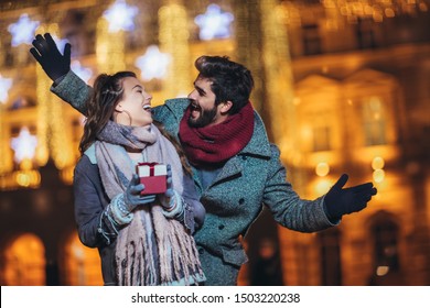 Young couple in the city centre with holiday's brights in background. Man presenting gift to woman. - Powered by Shutterstock