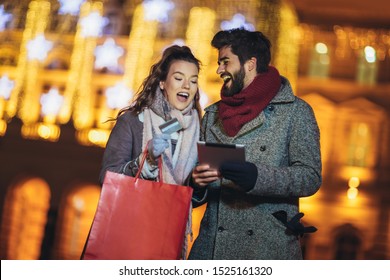 Young couple in the city centre with holiday's brights in background. Couple browsing digital tablet. They are using credit card for online shopping. - Powered by Shutterstock