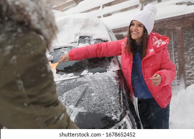 Young Couple Cleaning Snow From Car Outdoors On Winter Day