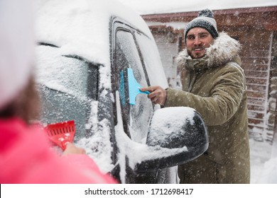 Young Couple Cleaning Snow From Car Outdoors On Winter Day