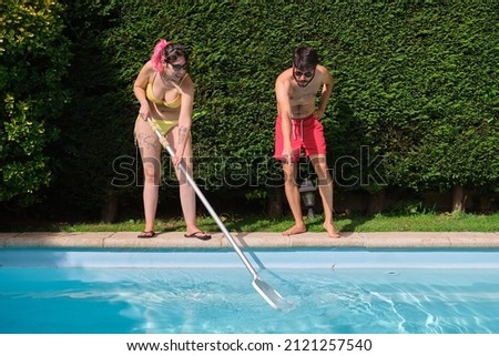 Young couple cleaning swimming pool of fall leaves with cleaning net.