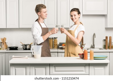 Young Couple Clinking With Glasses Of Milkshake In Kitchen