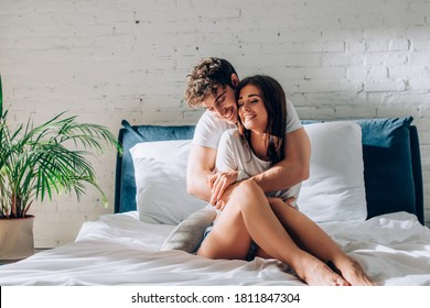 Young couple with closed eyes sitting on bed and embracing each other