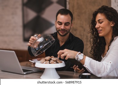 Young couple with coffee in cafe eating cookies